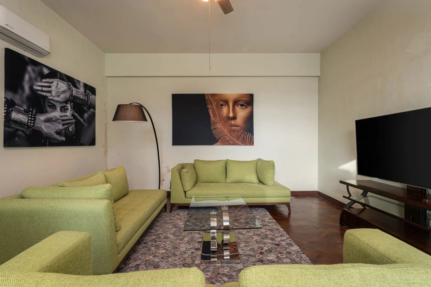 Una sala de estar con asientos verdes, una alfombra estampada y un televisor.