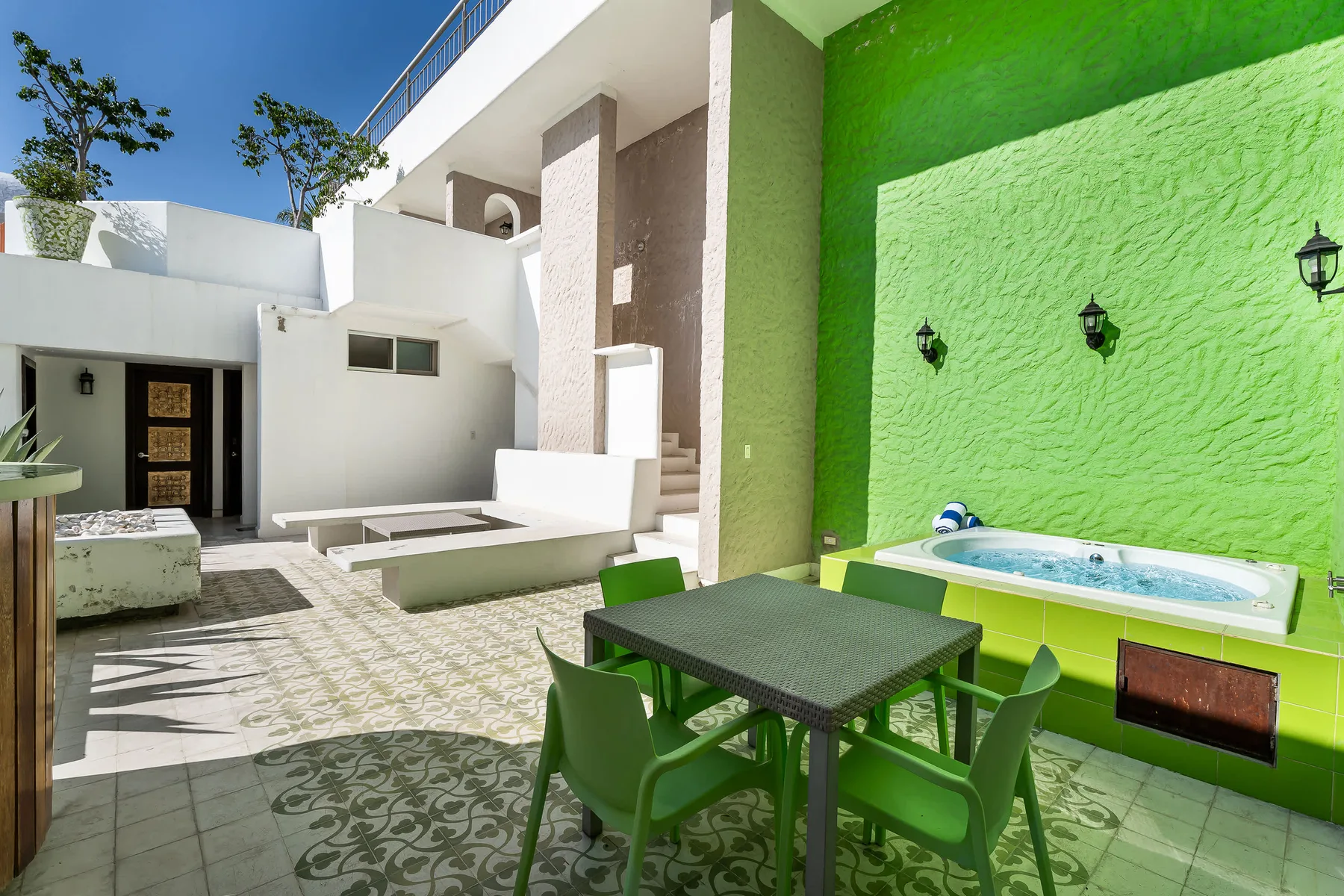 Un patio al aire libre con una mesa de comedor y una pequeña piscina junto a una pared verde brillante.