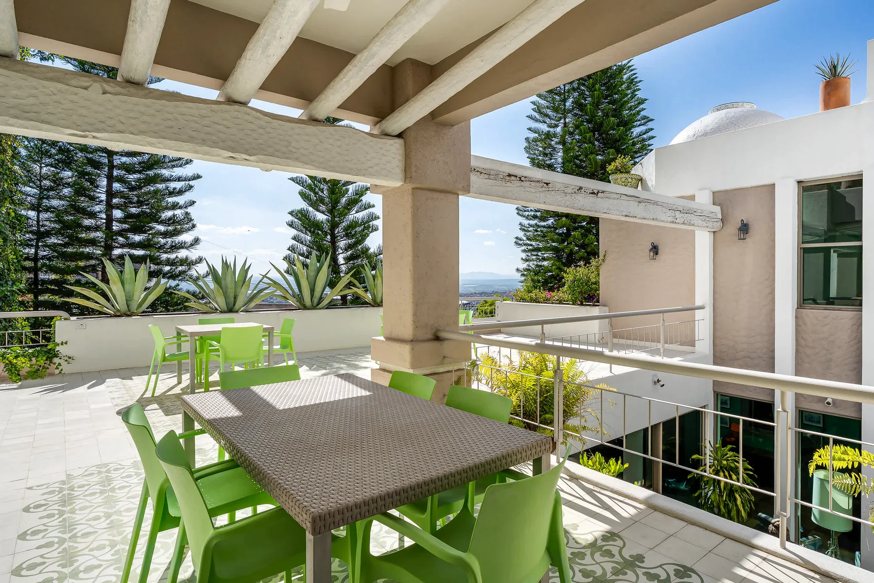 Una terraza soleada con asientos verdes bajo una pérgola.