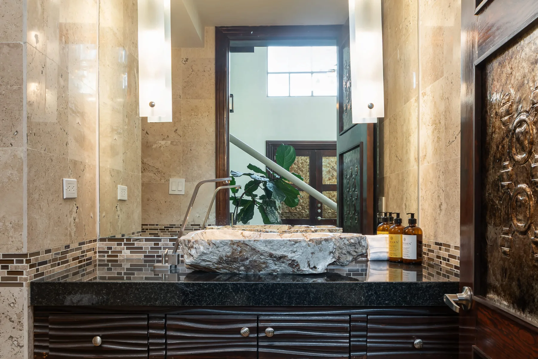 Un lavabo de baño con una pila de piedra y un espejo grande.