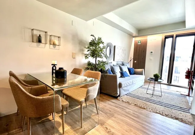 Una sala de estar con mesa de comedor y asientos junto a grandes ventanas.