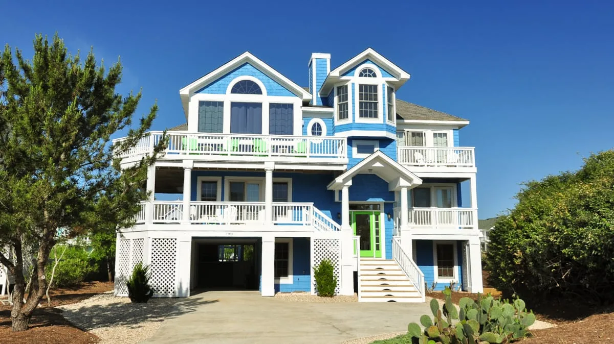 Una casa grande azul y blanca con balcones y una entrada para vehículos al frente.