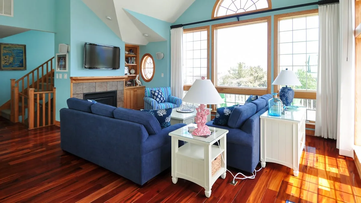 A bright living room with blue seating arranged around a coffee table beside large windows.