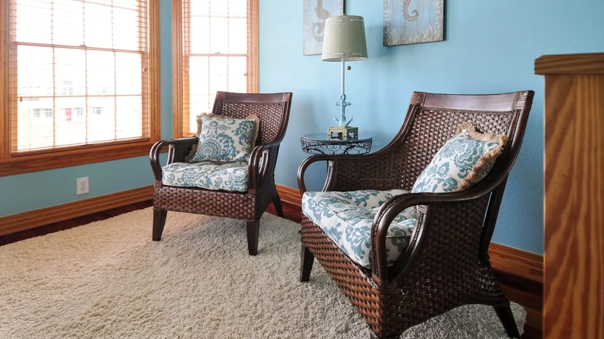 A sitting area with woven seating, patterned cushions, and large windows.