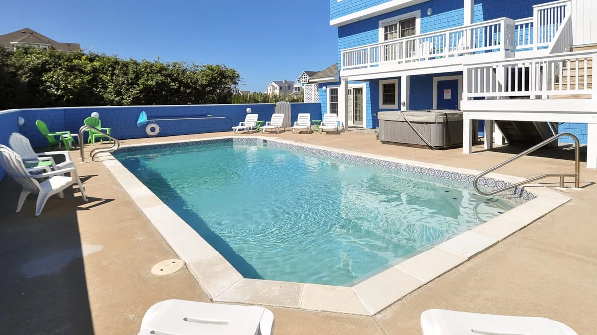 An outdoor swimming pool sits beside a blue building with white railings.