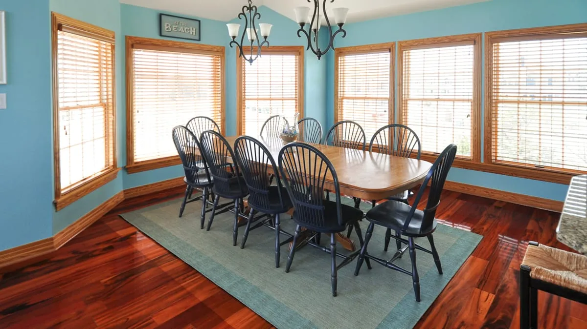 A dining room with a long wooden table and dark chairs beneath a chandelier.