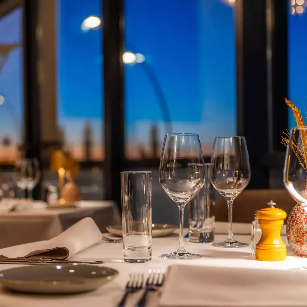 Espacio representativo del hotel: Una mesa de restaurante está preparada con copas y platos junto a grandes ventanas.