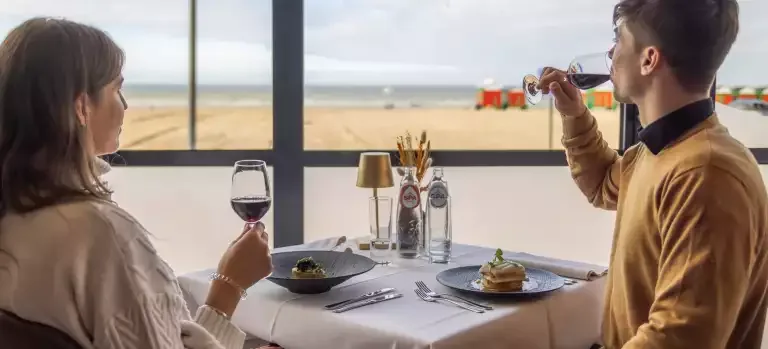 Espacio representativo del hotel: Una pareja comparte una comida en una mesa junto a una ventana amplia con vistas a la playa.