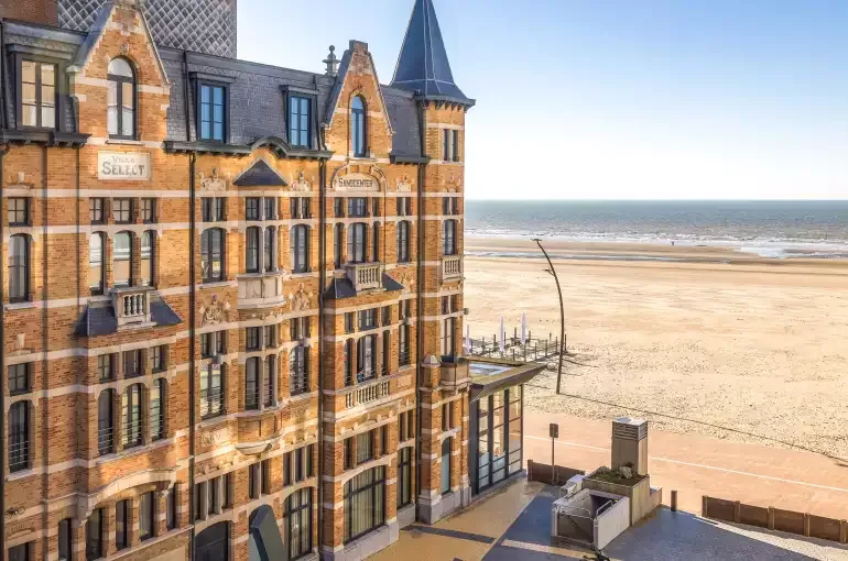 Espacio representativo del hotel: Un edificio hotelero de ladrillo está junto a una amplia playa de arena.