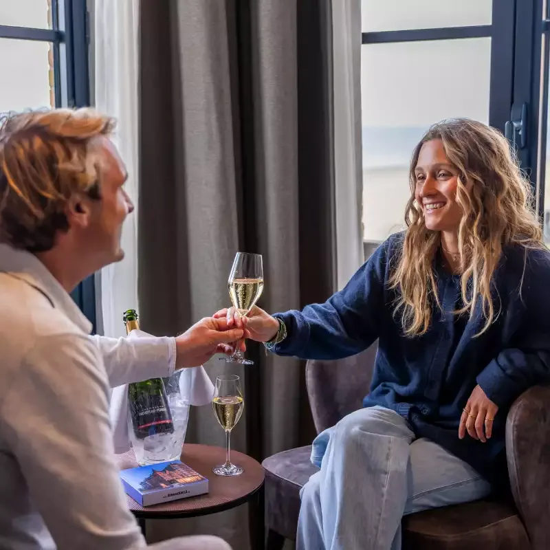 Espacio representativo del hotel: Dos personas brindan con vino mientras están sentadas junto a una ventana.