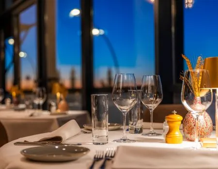 Espacio representativo del hotel: Mesa de restaurante preparada con cristalería y vajilla junto a ventanales.