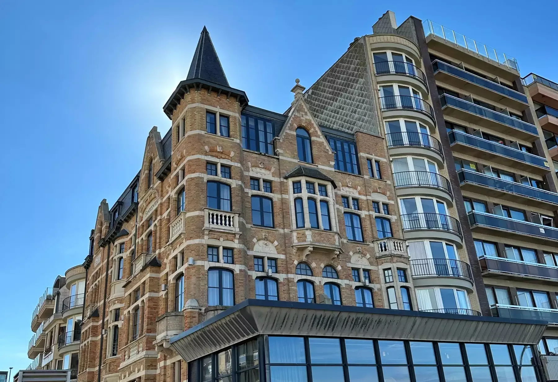 Espacio representativo del hotel: Un edificio de ladrillo ornamentado está junto a un edificio moderno bajo un cielo azul despejado.