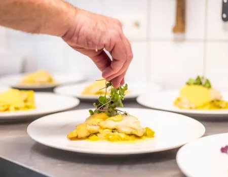 Espacio representativo del hotel: Una mano decora platos servidos con hierbas frescas en una cocina.