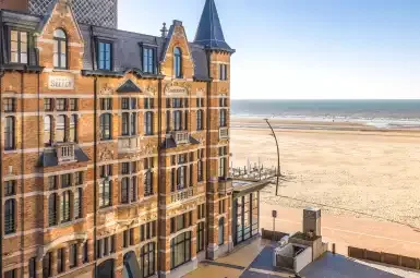 Espacio representativo del hotel: Un edificio de ladrillo con secciones de techo puntiagudas se alza junto a una amplia playa de arena.