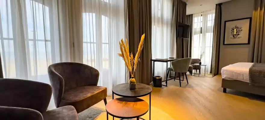 Espacio representativo del hotel: Una habitación de hotel tiene una cama, asientos y una mesa redonda junto a ventanas altas.
