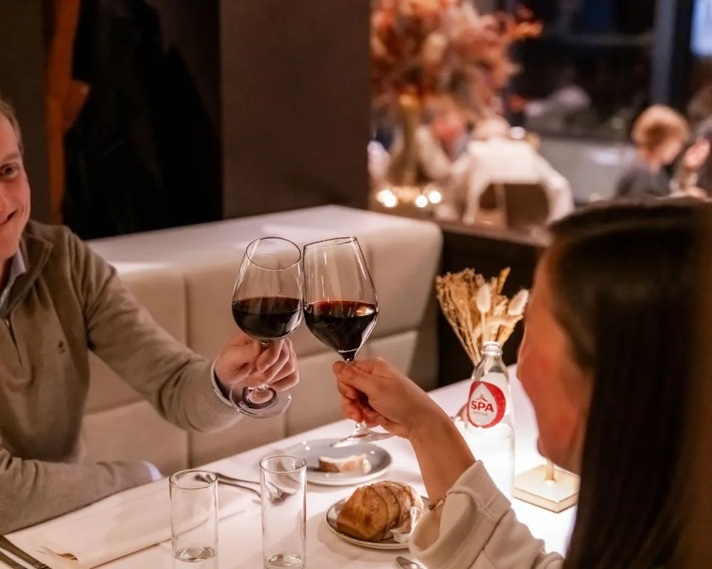 Espacio representativo del hotel: Escena de restaurante con dos personas brindando con copas de vino en una mesa.