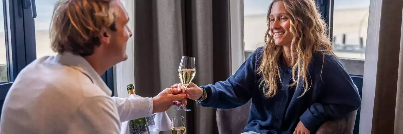 Espacio representativo del hotel: Un hombre y una mujer brindan con copas de champán junto a una ventana.