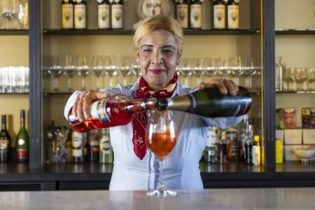 Espacio representativo del hotel: Una camarera sirve bebidas detrás de una barra con botellas y vasos.