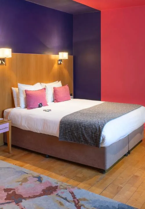 Representative hotel space: A bedroom with a neatly made bed, colorful pillows, and bold accent walls.