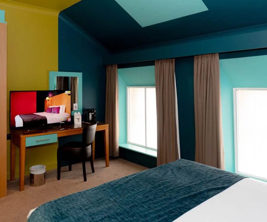 Representative hotel space: A colorful bedroom with a bed, desk, and bright windows.