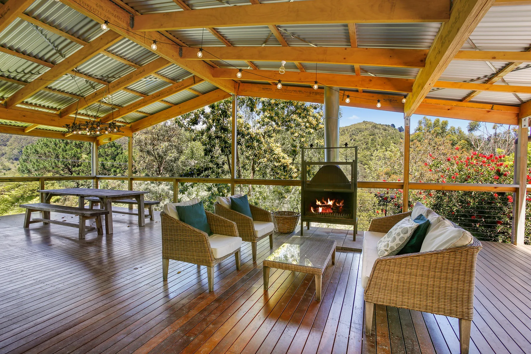 A covered outdoor seating area has wicker chairs, a table, and a fireplace.