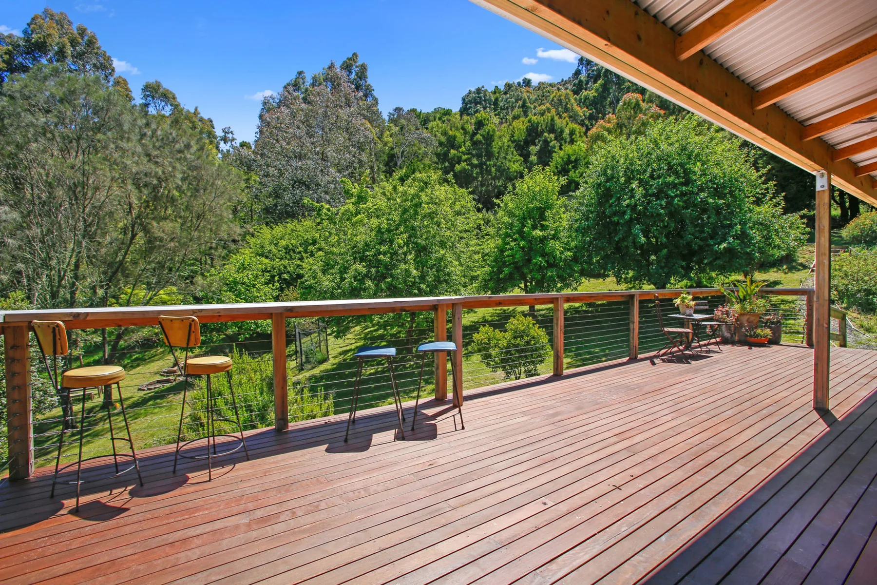 A covered wooden deck overlooks a green, tree-covered hillside.