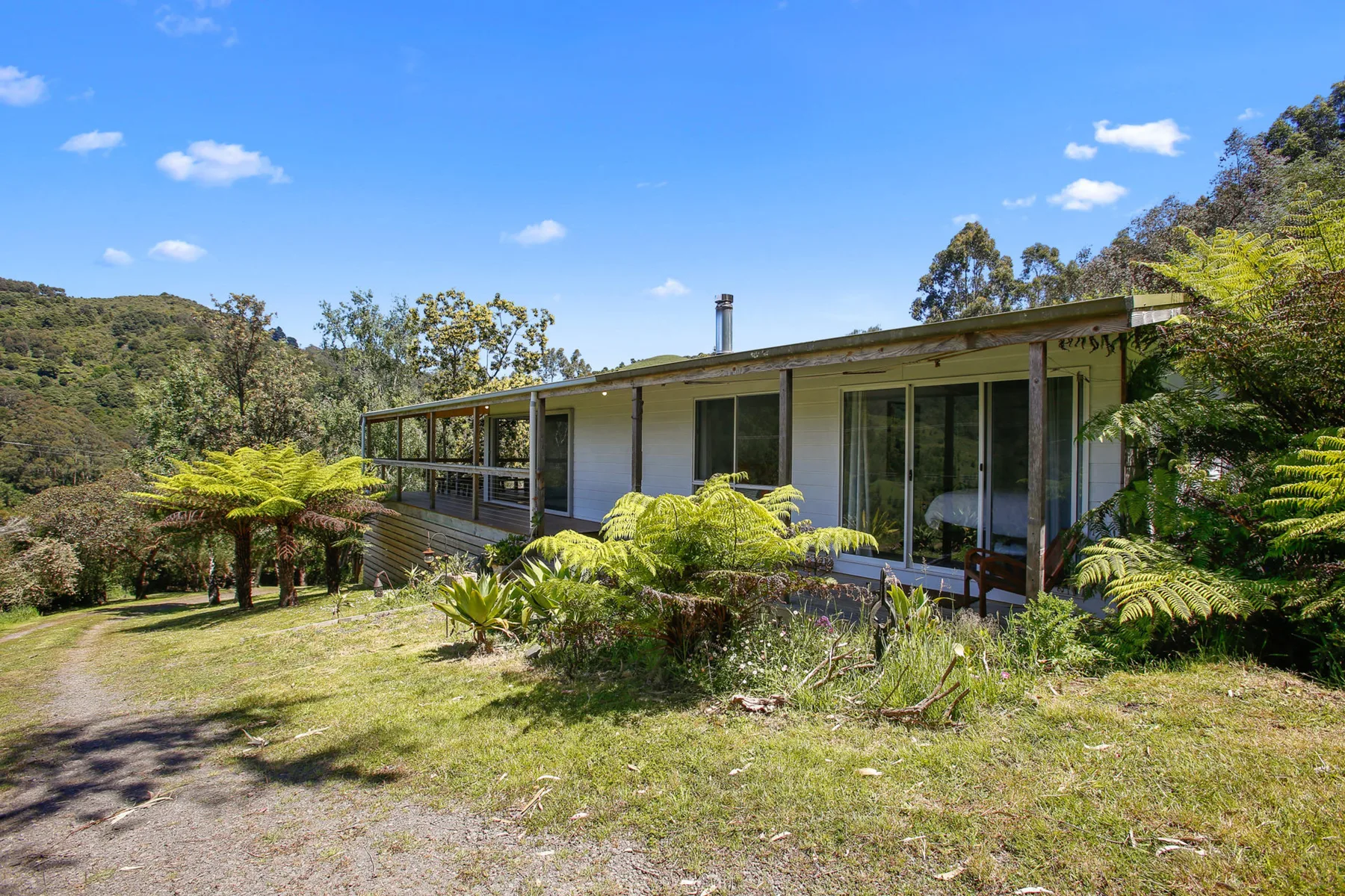 A modern house sits among landscaped greenery beneath a clear blue sky.