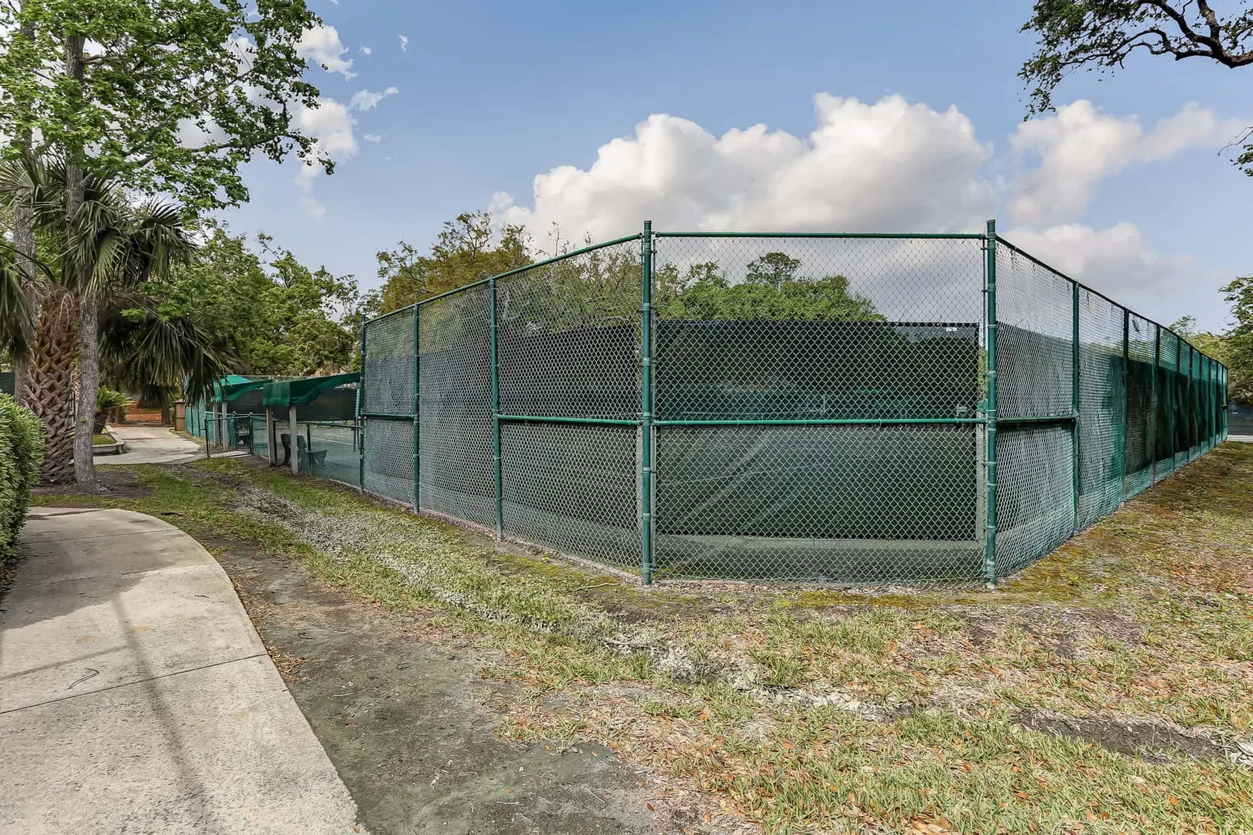 Shared amenity: A fenced outdoor sports court beside a paved walkway and trees.
