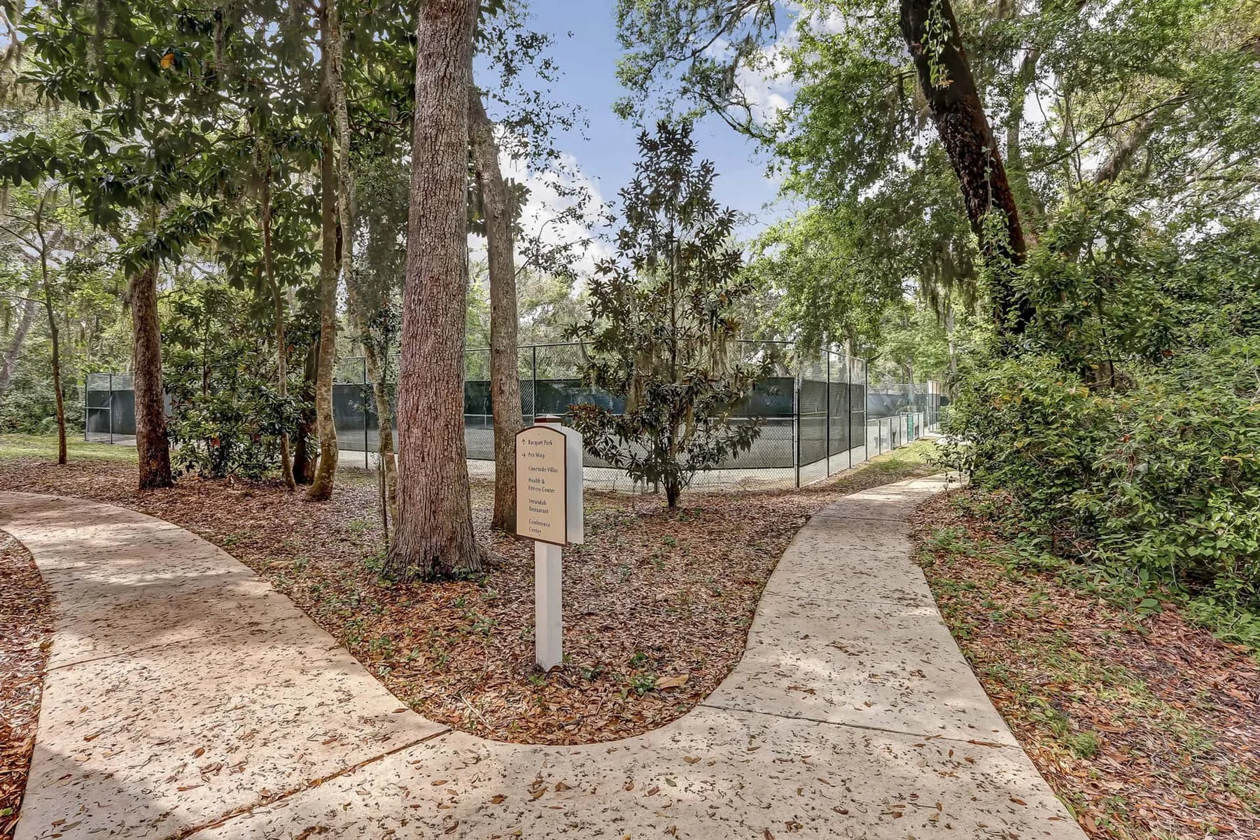 Shared amenity: A paved path curves through a wooded area beside a fenced court.