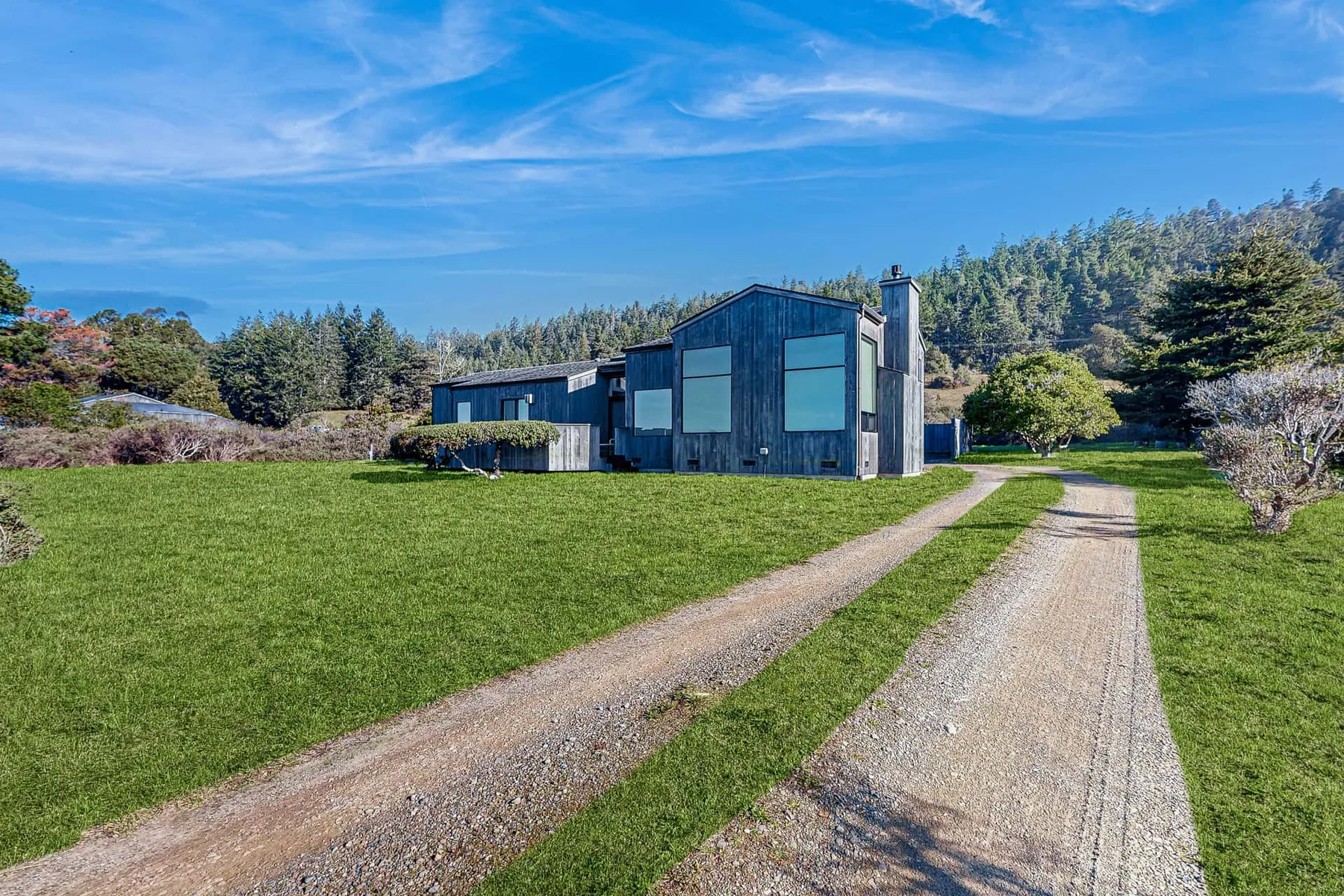 A modern house sits beside a gravel driveway and broad green lawn.
