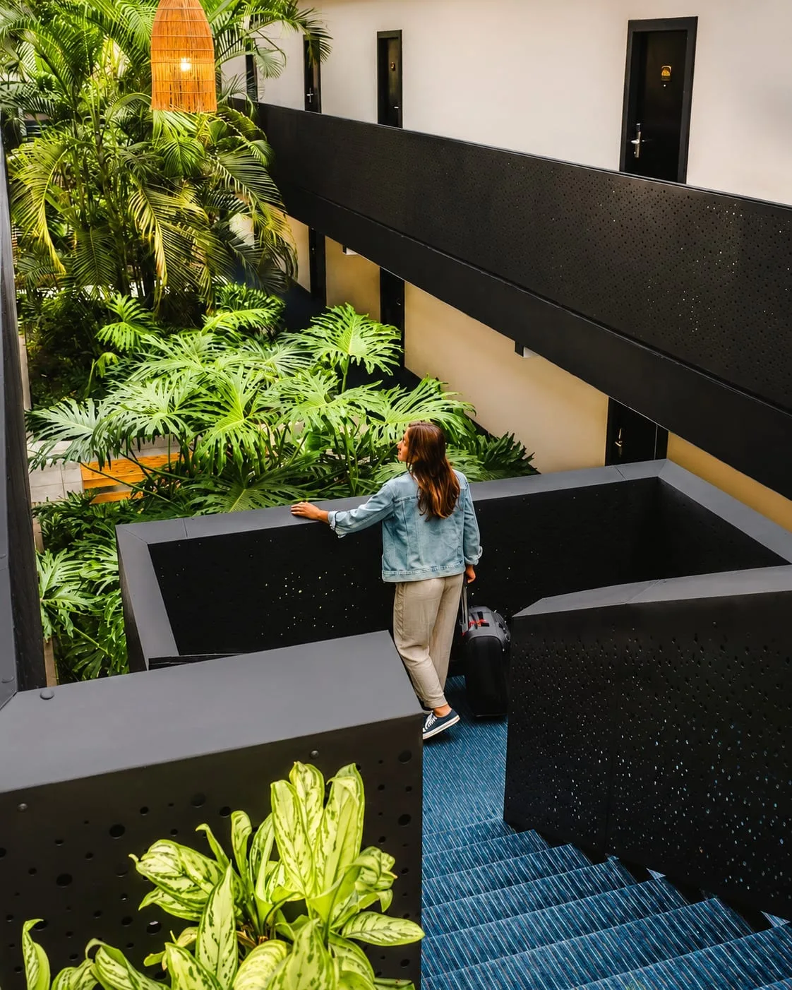 Representative hotel space: An indoor stairway overlooks a leafy courtyard with a person descending the steps.