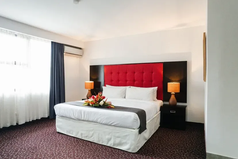 Representative hotel space: A bedroom with a large bed, red headboard, and curtained window.