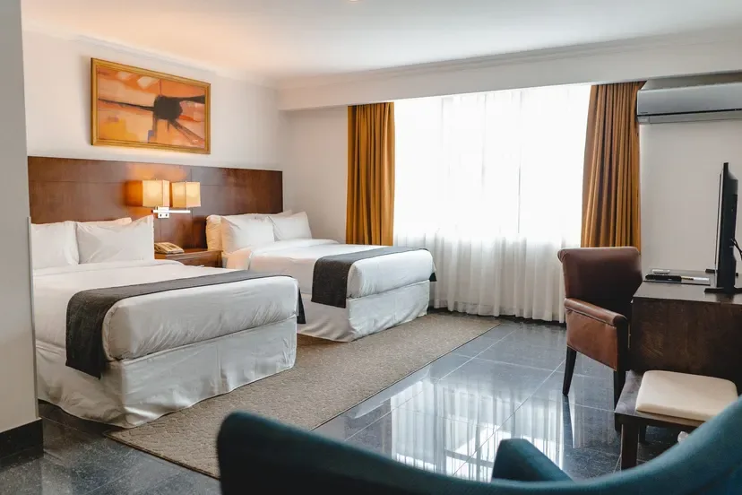 Representative hotel space: A hotel bedroom with two beds, a bright window, and a television.