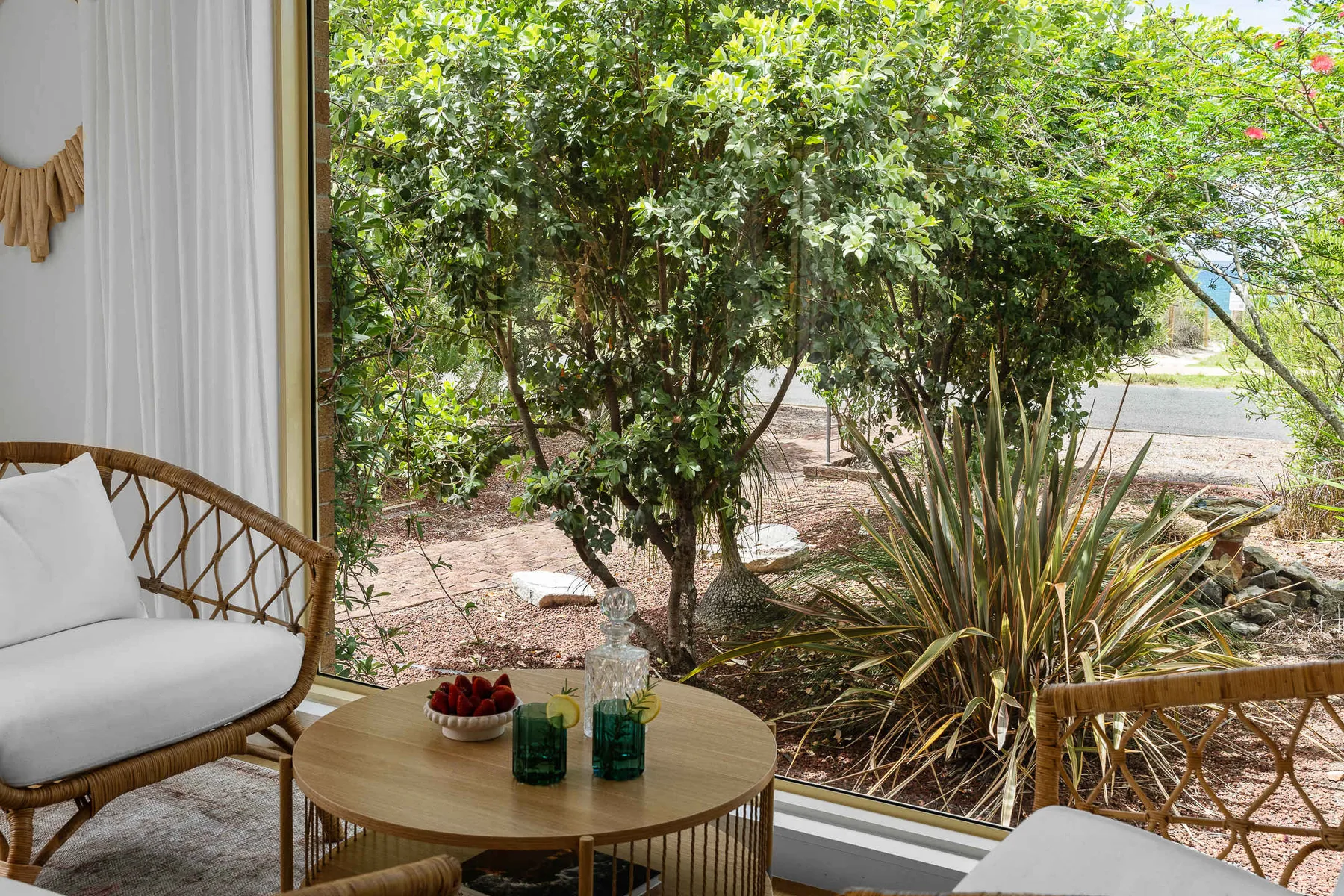 A bright sitting area opens onto leafy trees, with seating and a small table.