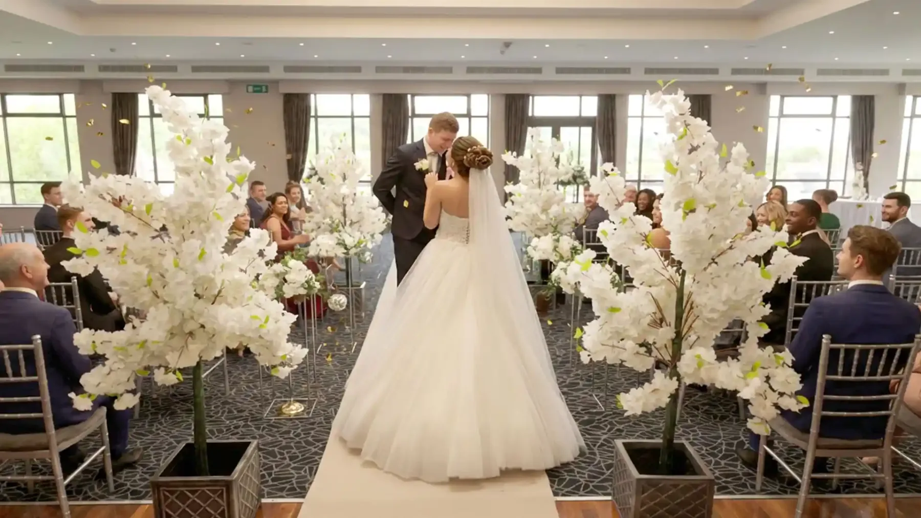Espacio representativo del hotel: Una novia y un novio están entre invitados sentados en un salón decorado para una boda.