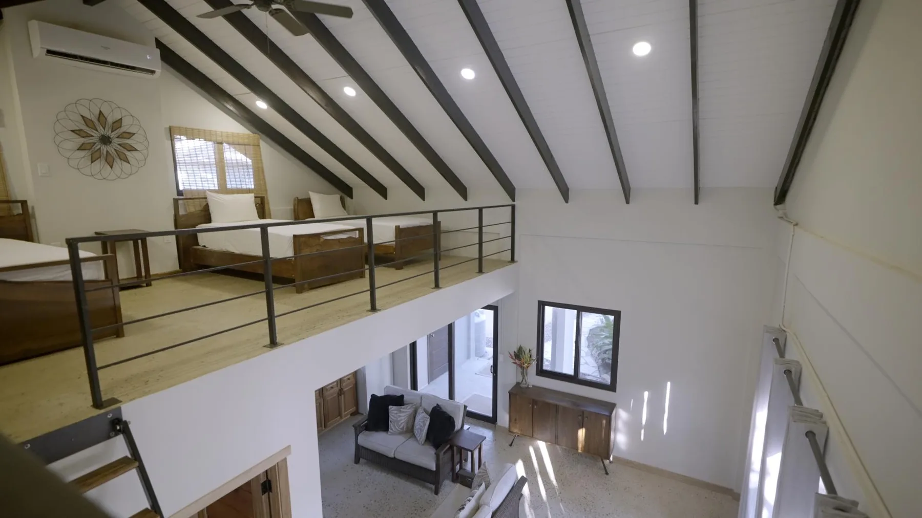 A bright loft living area with exposed ceiling beams and seating below.