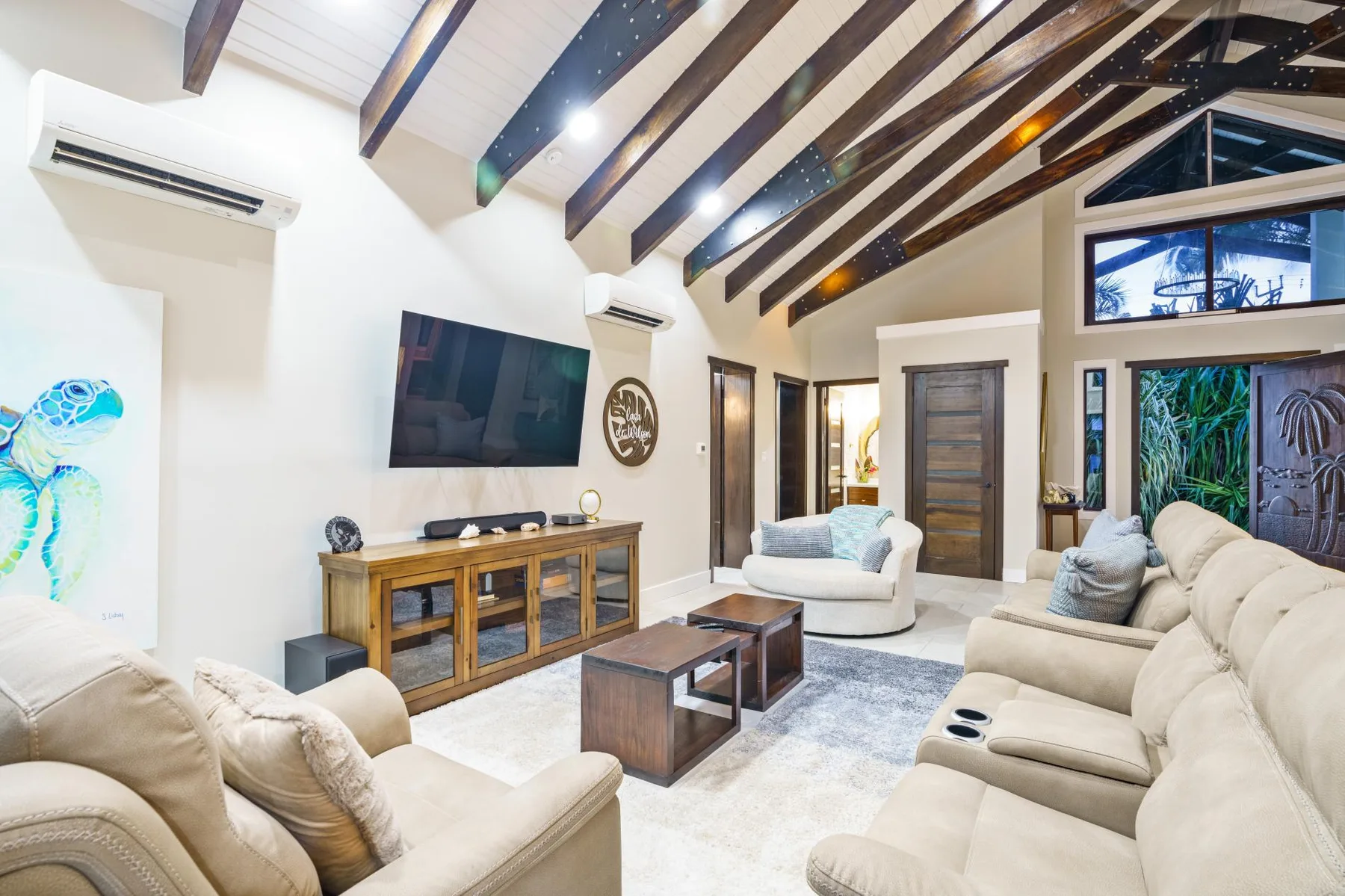 A bright living room with upholstered seating, a television, and exposed ceiling beams.