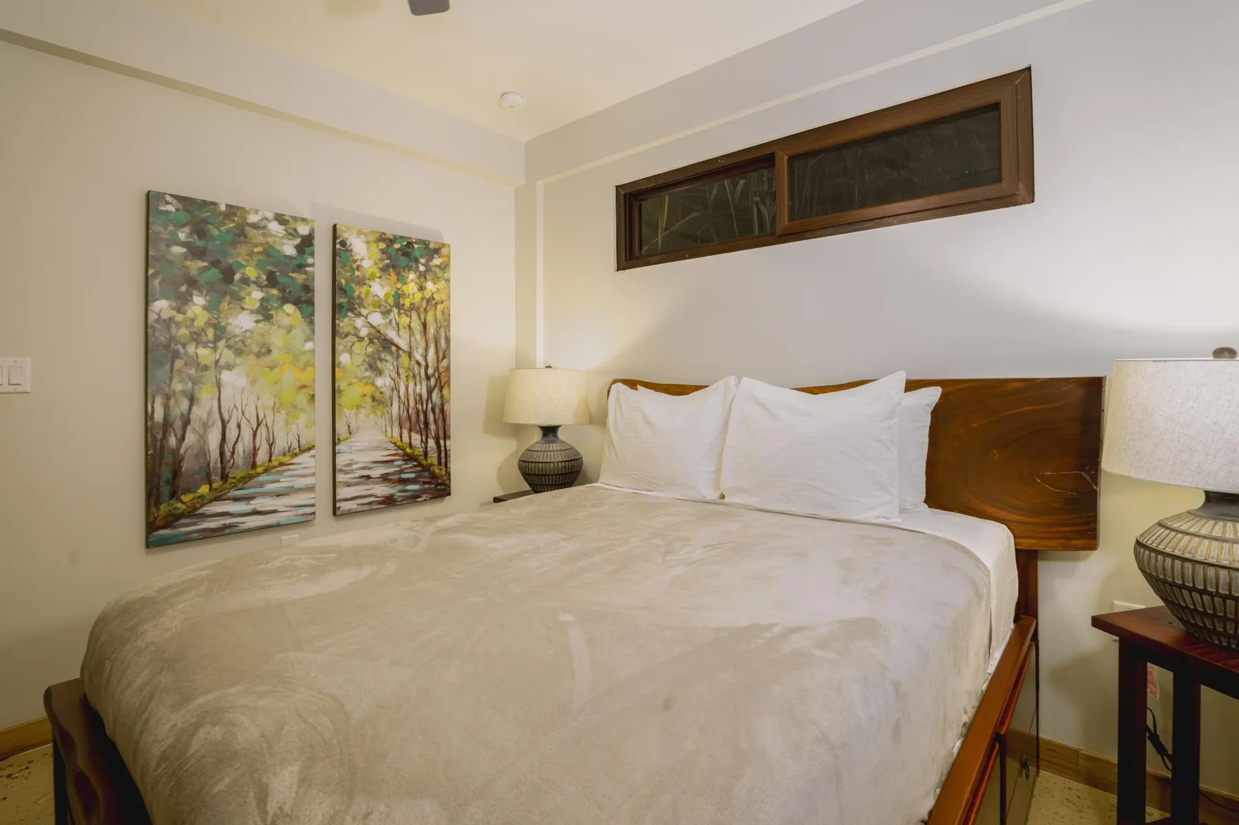 A bedroom with a bed, white pillows, and landscape paintings on the wall.