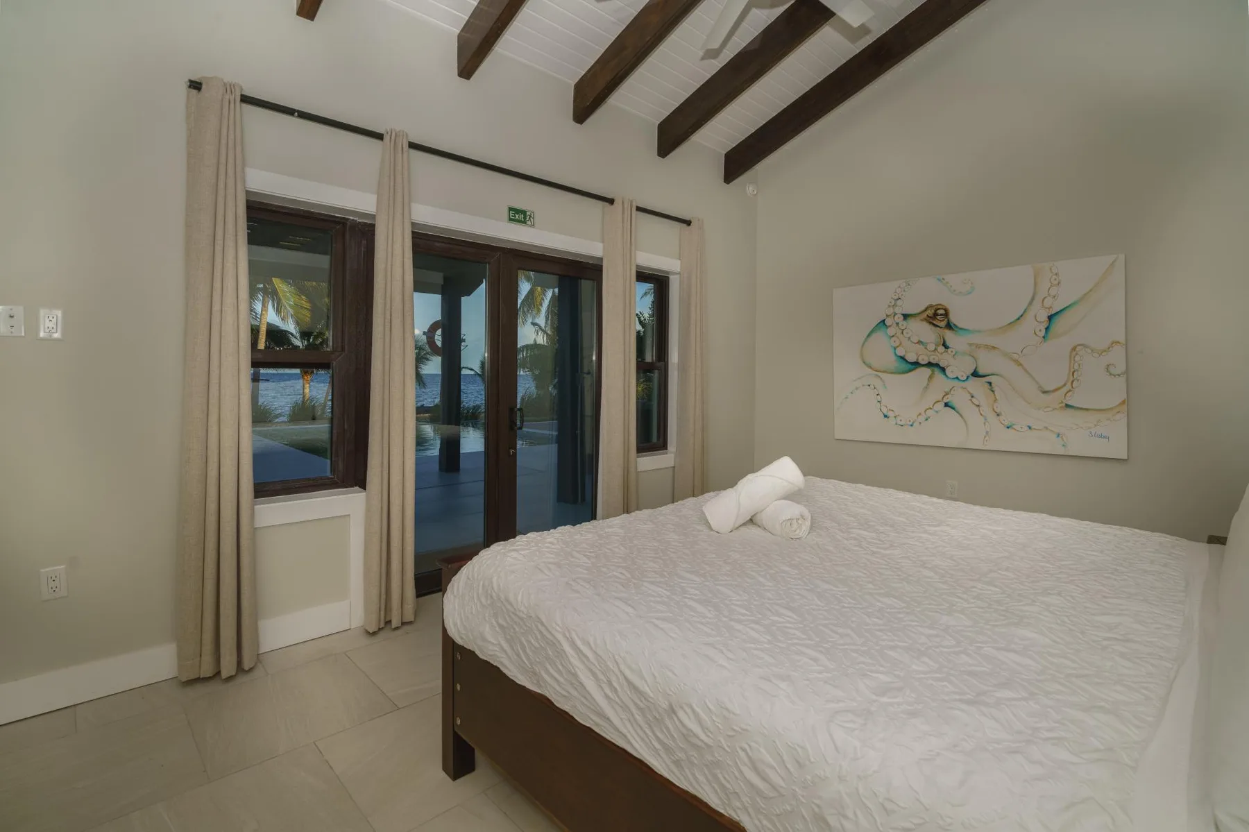 A bedroom with a large bed, light curtains, and artwork on the wall.