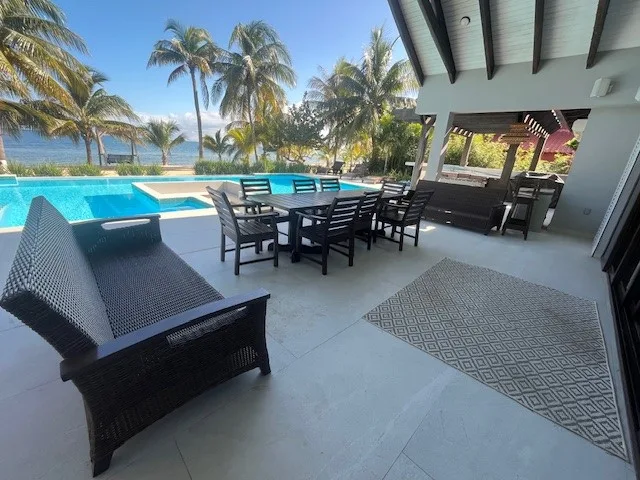 A covered patio with dining seating overlooks a swimming pool and palm trees.