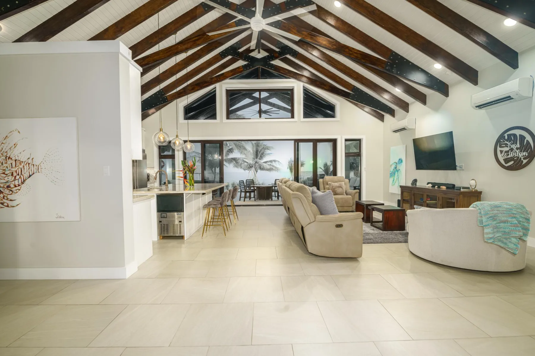 A spacious open-plan living room with seating and a kitchen beneath exposed beams.
