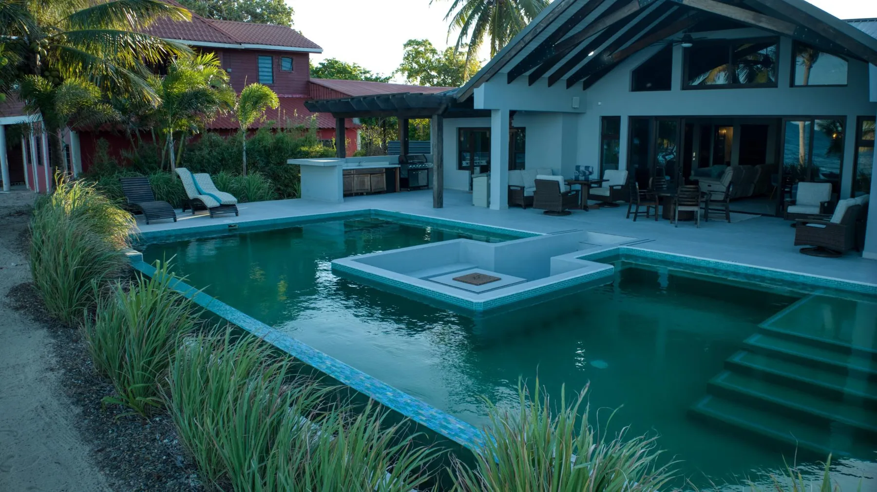 An outdoor swimming pool beside a modern building, with lounge seating nearby.
