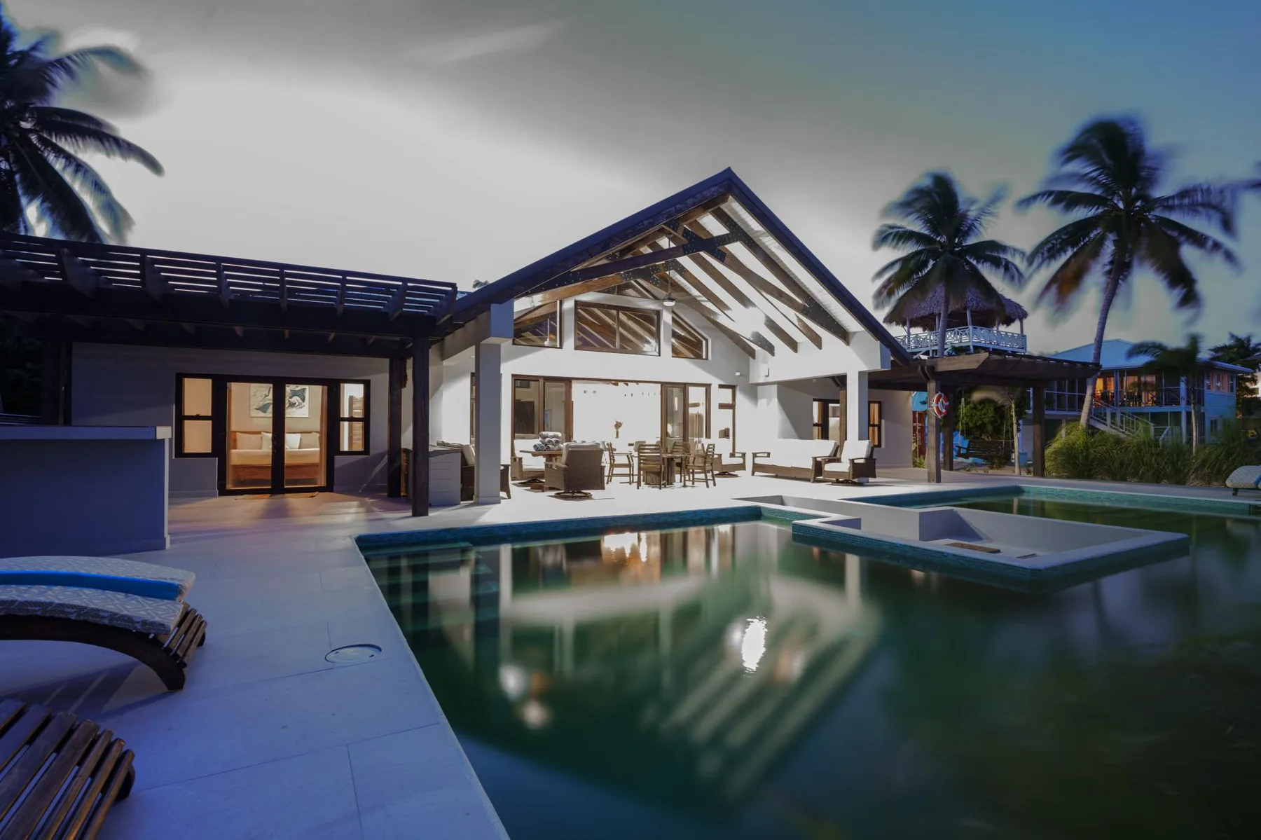 A modern house opens onto a swimming pool, with palm trees in the background.