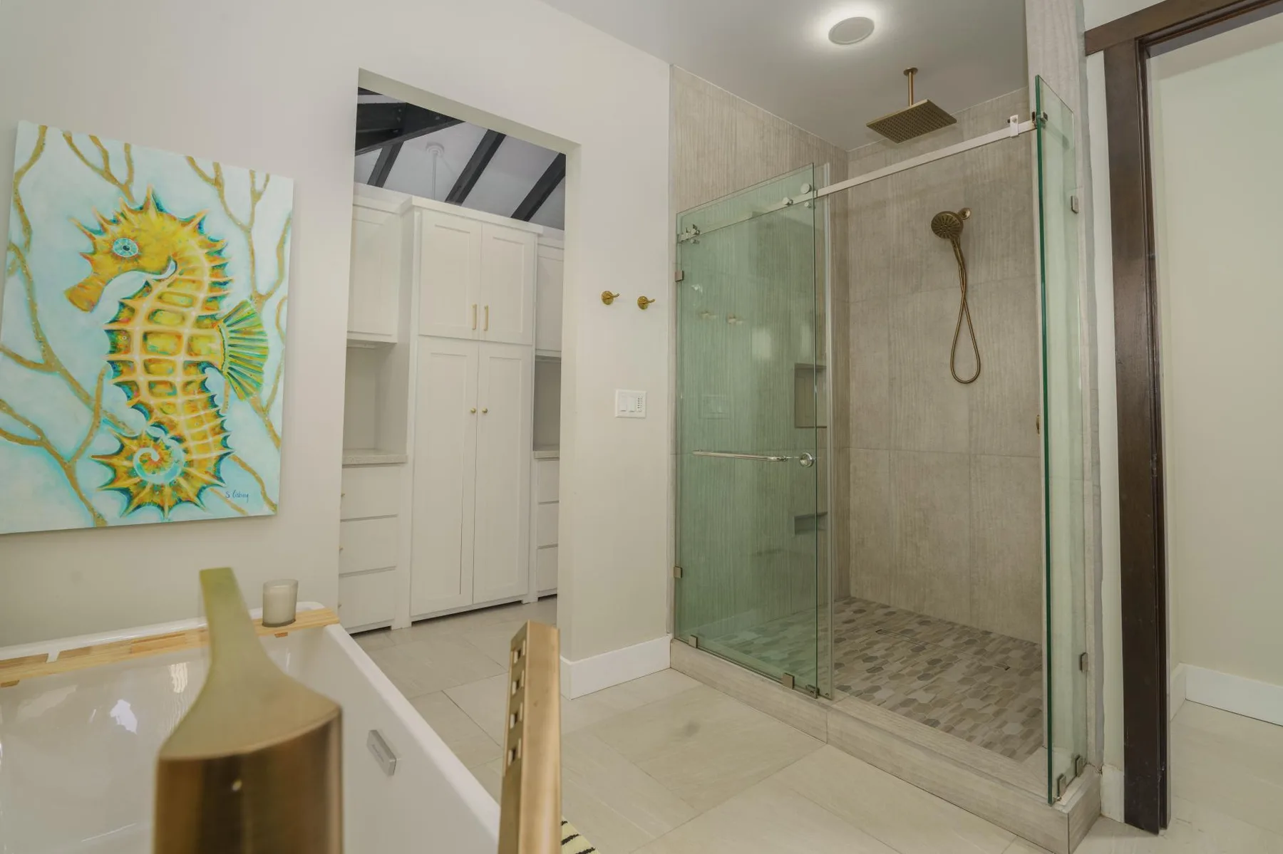 A bathroom with a glass shower and colorful seahorse artwork on the wall.