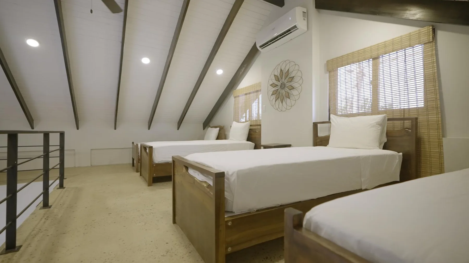 A bright bedroom with several beds and sloped ceilings with exposed beams.