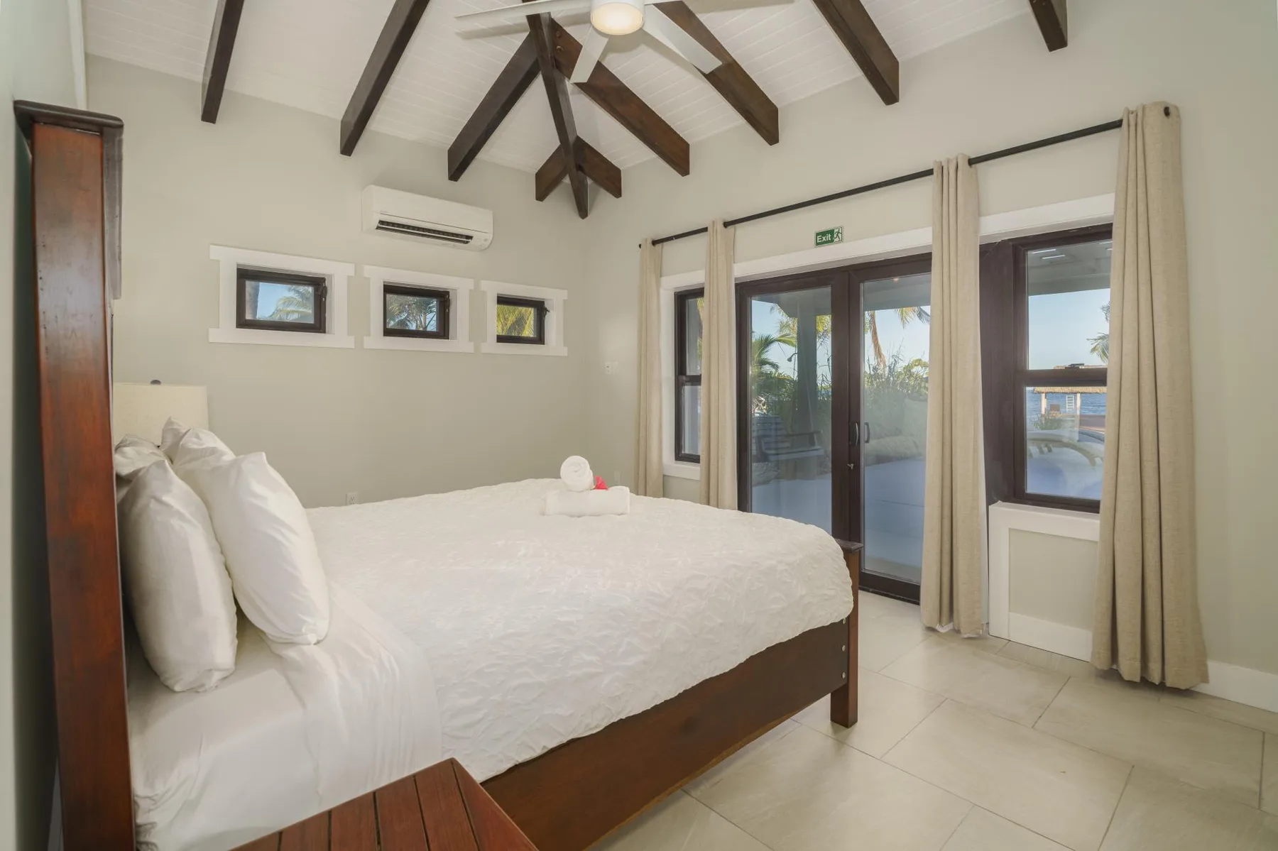 A bedroom with a large bed, exposed ceiling beams, and glass doors.