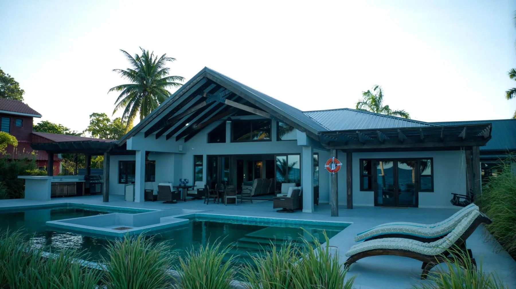 A modern house opens onto a swimming pool, with lounge seating beside the water.