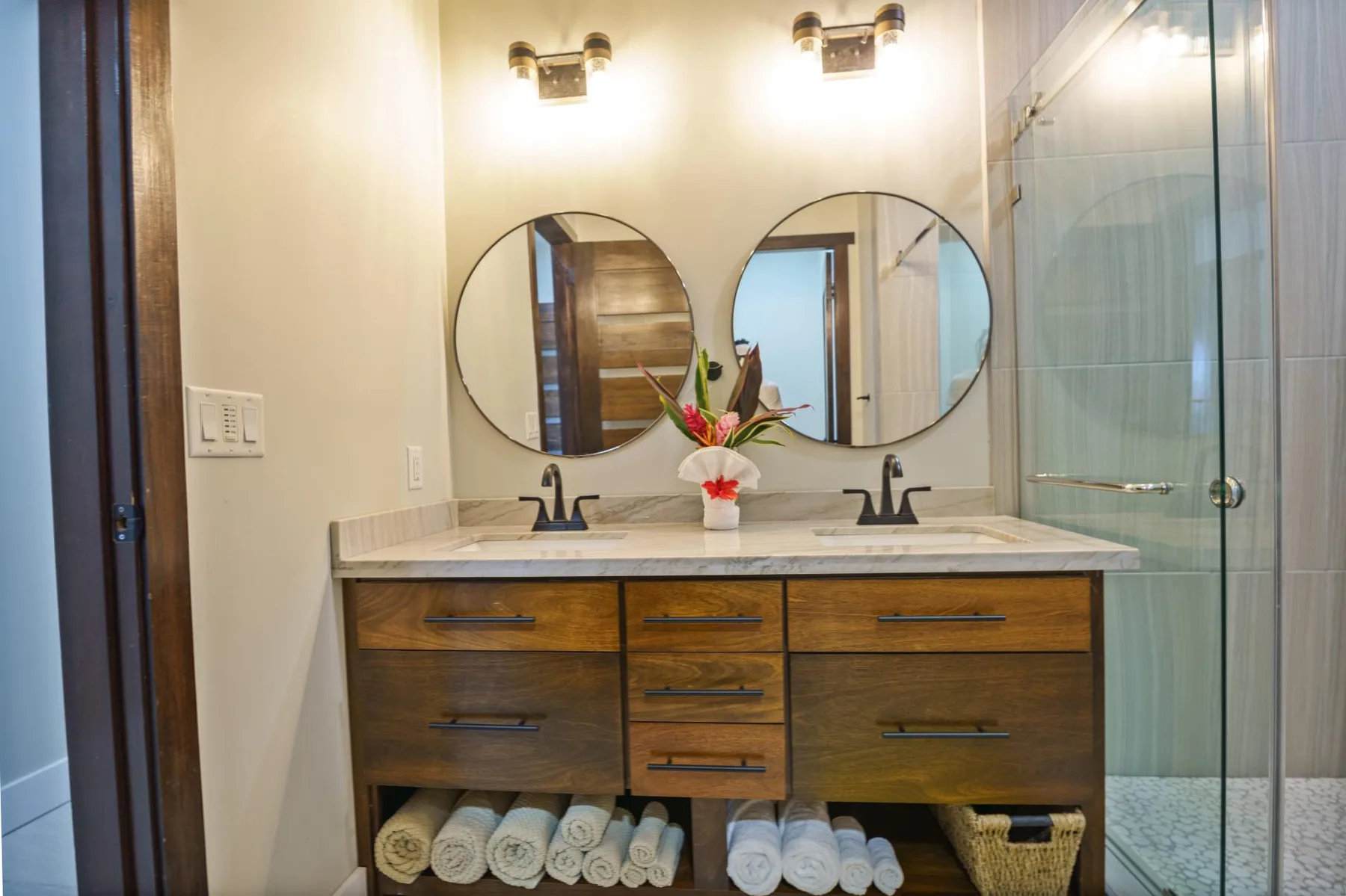 A bathroom vanity with twin round mirrors and a glass shower.