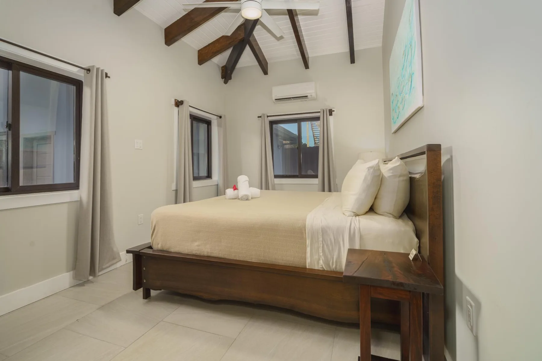 A bedroom with a neatly made bed beneath exposed ceiling beams.
