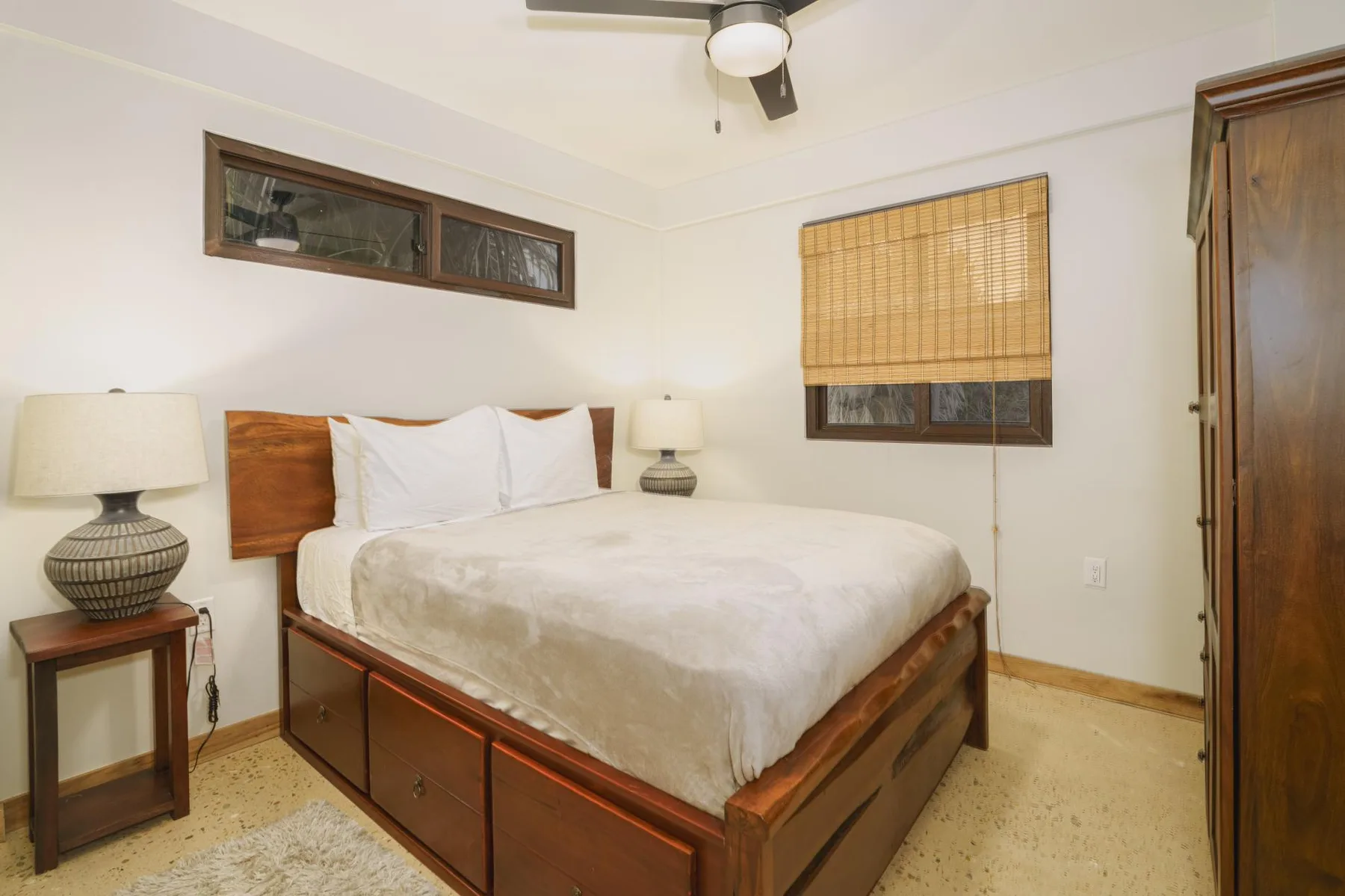 A bedroom with a wooden bed, white bedding, and windows with blinds.